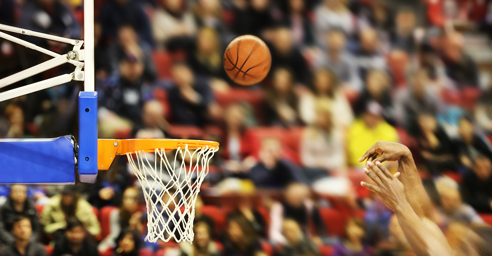 Basketball going into hoop on court with people in the bleachers watching